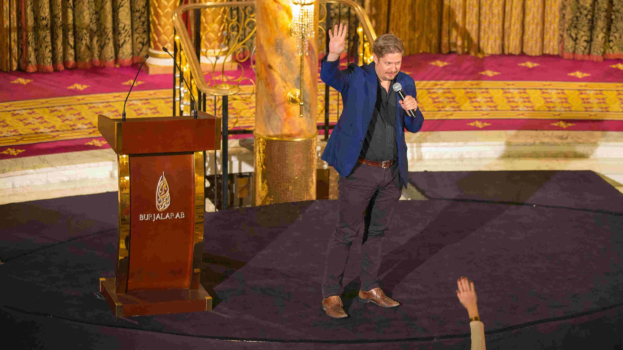 Oskar Andermo speaking on stage at Burj Al Arab in Dubai, microphone in hand and one arm raised towards the audience